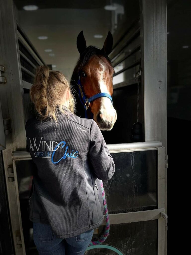 A Woman Gently Pets a Brown Horse in a Wooden Stall.