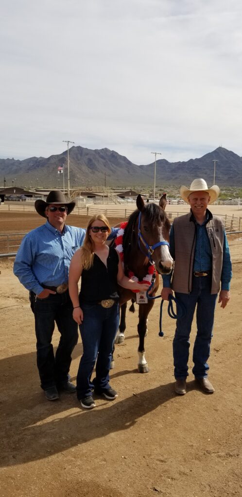 Three Individuals Standing Beside a Horse in a Dusty Field.
