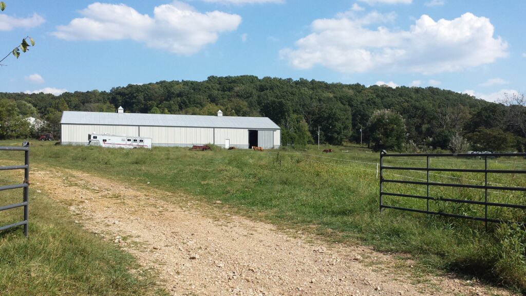 A Dirt Road Leading to a Gate and a Barn in the Countryside.