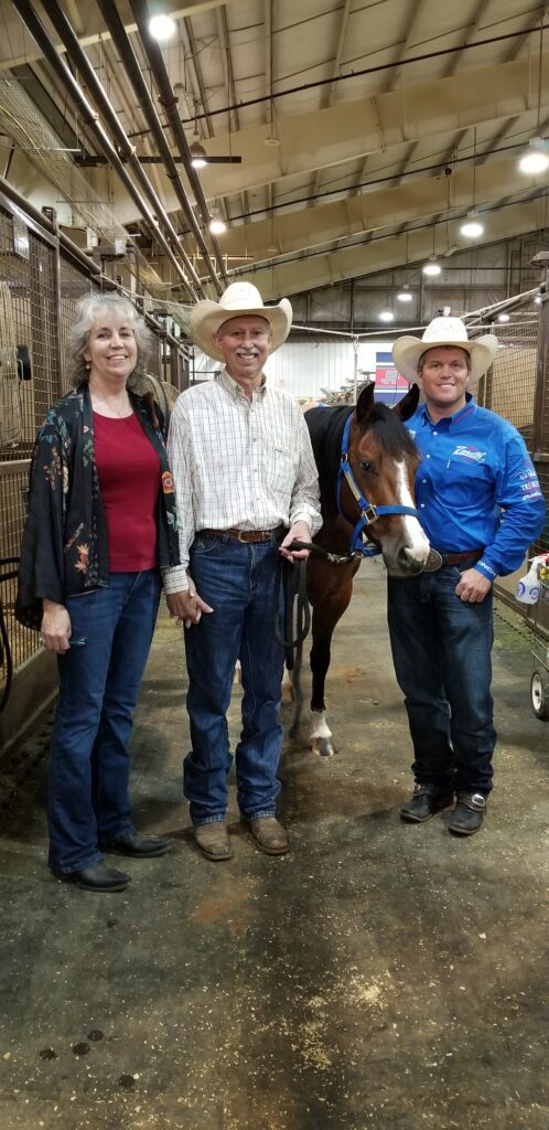 A Man and Two Women Standing Next to a Horse in a Field.