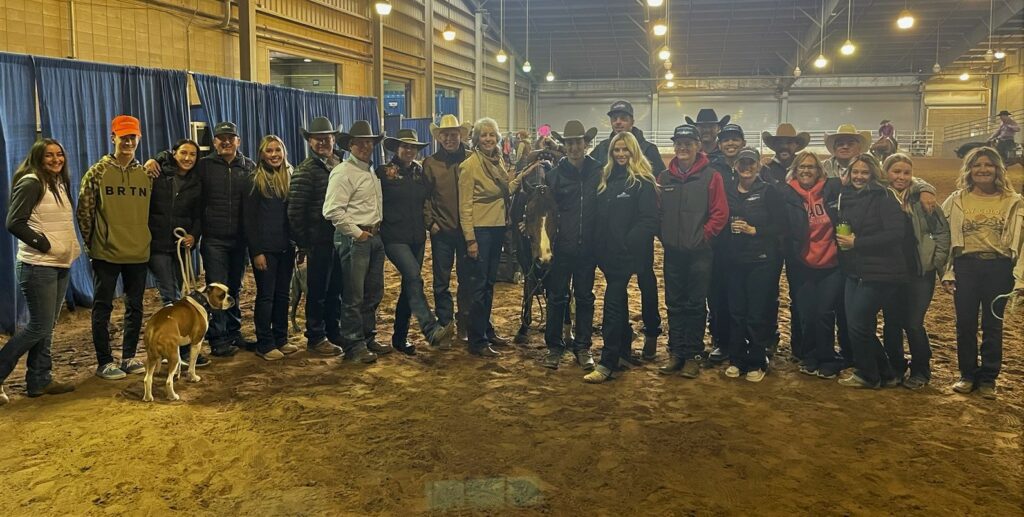 A Group of People Standing in an Indoor Arena With a Dog, Surrounded by a Lively Atmosphere.