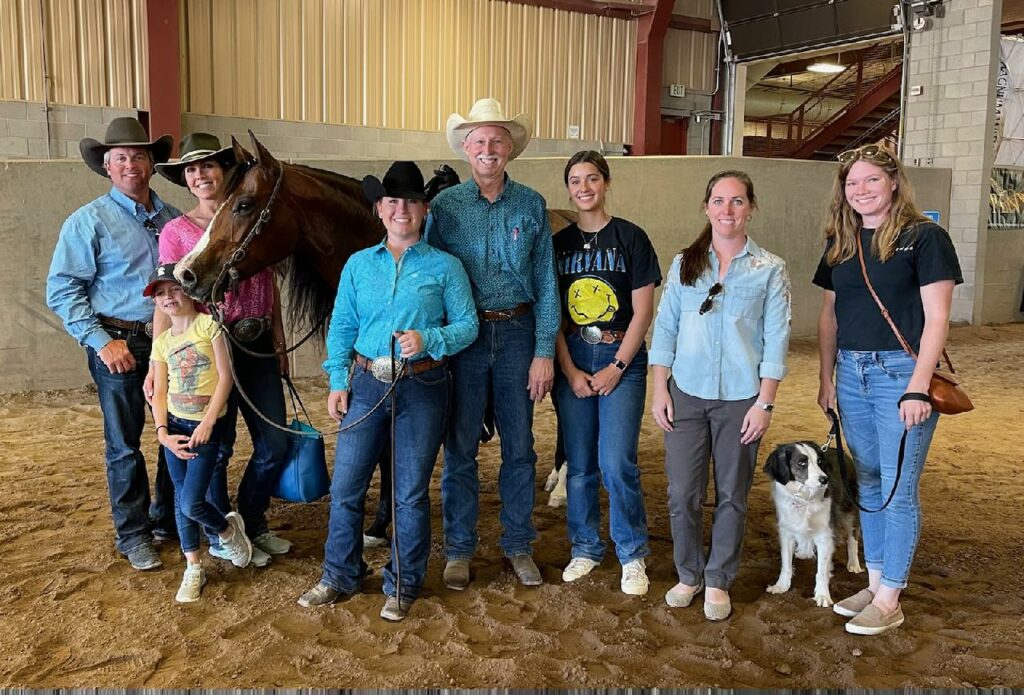 A Group of People and a Horse Standing in an Arena, Surrounded by a Fence, Under a Clear Blue Sky.